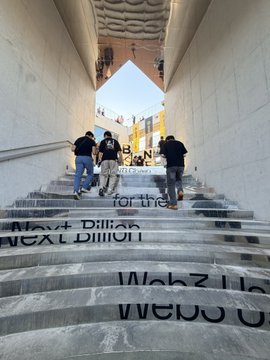 People walking up a set of stairs with motivational text including "Make Billions", "Next Billion", and "Wahz I go" projected on the steps.