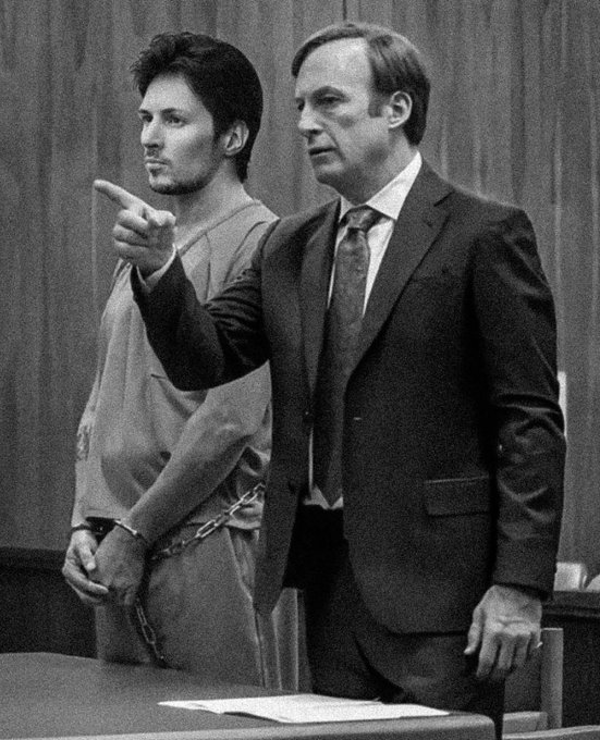 Black and white courtroom photo showing a younger man in a beige prison jumpsuit pointing while an older man in a dark suit stands beside him.