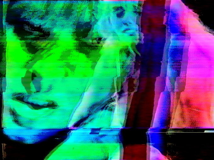 A distorted, glitch-art style image of a face overlaid with vibrant green, pink, and blue colors and horizontal scan lines.
