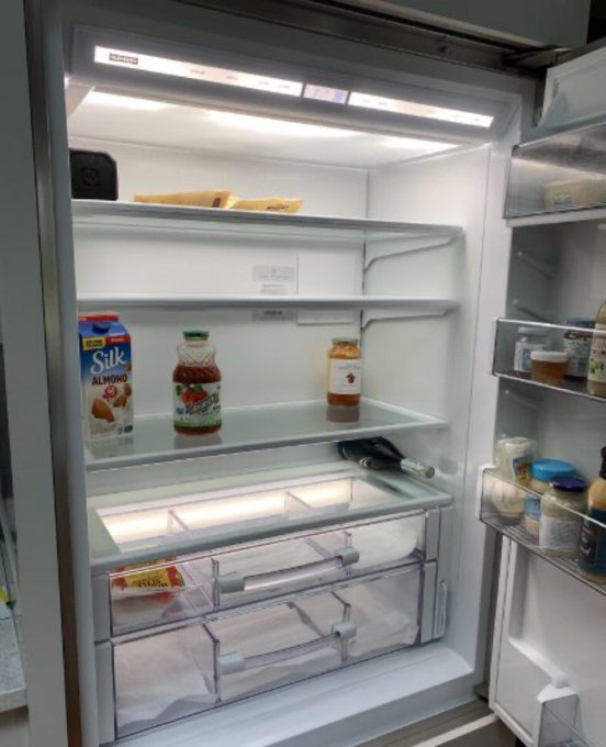 A nearly empty refrigerator containing Silk Almond milk, a bottle of juice, a small jar, and various condiments on the door shelves.