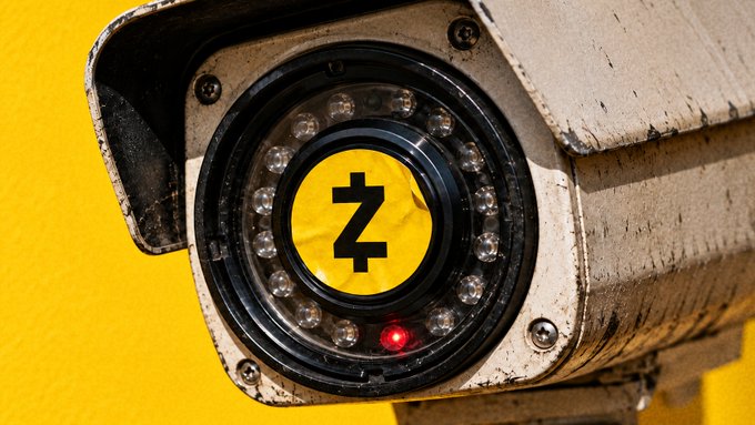 A close-up of a CCTV security camera with a yellow sticker featuring a 'Z' symbol over the lens, set against a yellow wall.