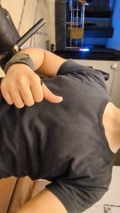 A close-up photo of a muscular person's thigh in dark shorts, with their hand making a downward thumbs-down gesture while wearing a dark glove.