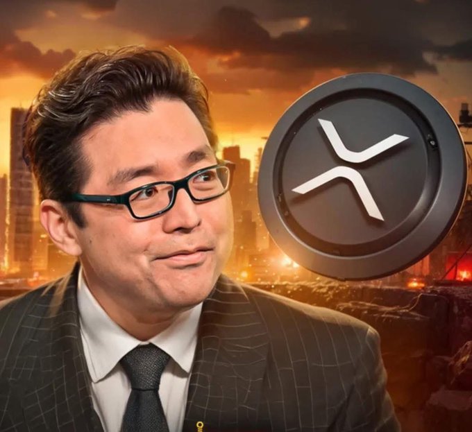 The image features a man wearing glasses, a suit, and a tie with an XRP symbol above his head. The background shows a city skyline at sunset, creating a dramatic atmosphere for the scene. The caption of the image reads "BOOOOOOOMMM!!!! TOM LEE JUST SAID WE ARE ABOUT TO SEE ONE OF THE COSMOS!!! IT'S COMING #XRP".