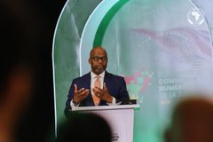 A man in a blue suit speaks at a podium during the Commonwealth Summit 2024, gesturing with his hand as he addresses the audience.