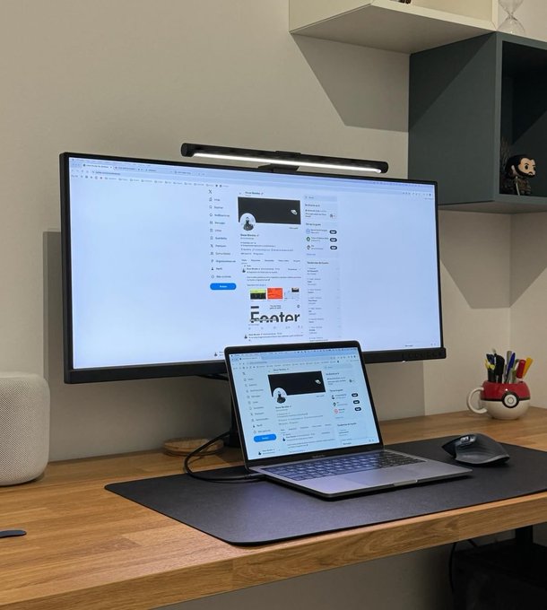 A desk setup featuring a large monitor and a laptop, both displaying the LinkedIn profile of 'Arsen Mkrt.', accompanied by a monitor light bar, an Apple HomePod, and a Pokéball mug.