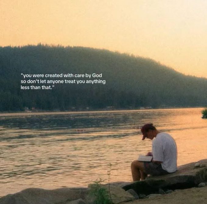 A young man sits by a lake at sunset writing in a notebook, with an inspirational quote overlaid: 'you were created with care by God so don't let anyone treat you anything less than that.'