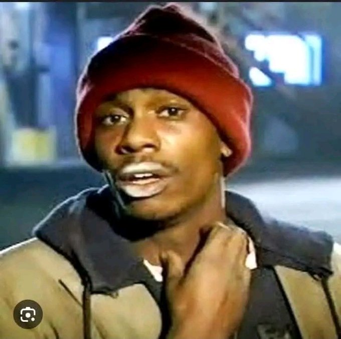 A close-up shot of a man wearing a red knit beanie and a tan jacket over a dark hoodie, standing outside at night.