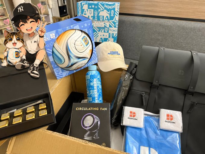 A cardboard box filled with assorted merchandise, including a soccer ball in a blue box, a white 'FAMOUS AQUATIC PAR' cap, a blue water bottle, a 'CIRCULATING FAN' box, a grey 'DEEPCOM' laptop bag, and branded towels, with a cartoon sticker overlay in the top left.
