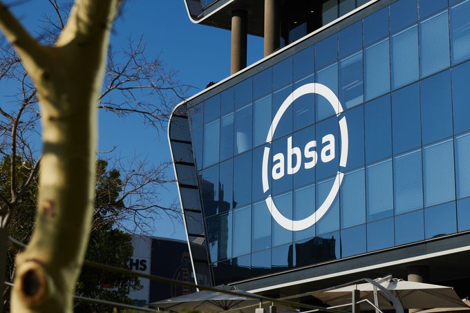 The exterior of a modern glass building displays a large white 'absa' logo, with a tree visible in the foreground against a clear blue sky.