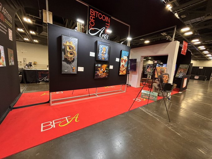 The image showcases a vibrant art exhibit at the **Midwest Bitcoin Summit**, featuring a booth titled "Bitcoin from the Arts" by @artbyshipwreck. The display includes colorful Bitcoin-themed artwork, including pieces like "GOLD" and "HODL," displayed on a black backdrop with a striking red carpet bearing the "BFTA" logo.