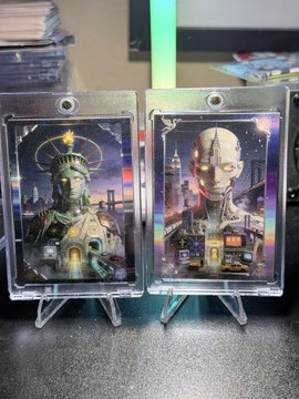 Two collectible cards displayed in protective cases on stands, featuring stylized artwork of a green-robed figure and a bald futuristic character.