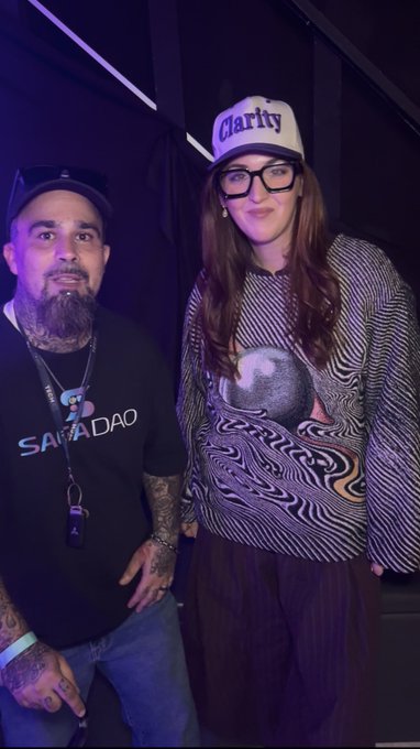 Two people pose together at the Solana Summer House event in Los Angeles—one wearing a black "SAGADAO" shirt and the other sporting a white "Clarity" cap and a patterned top—reflecting the post's mention of SagaDAO and RachelOnchain connecting at the crypto gathering.