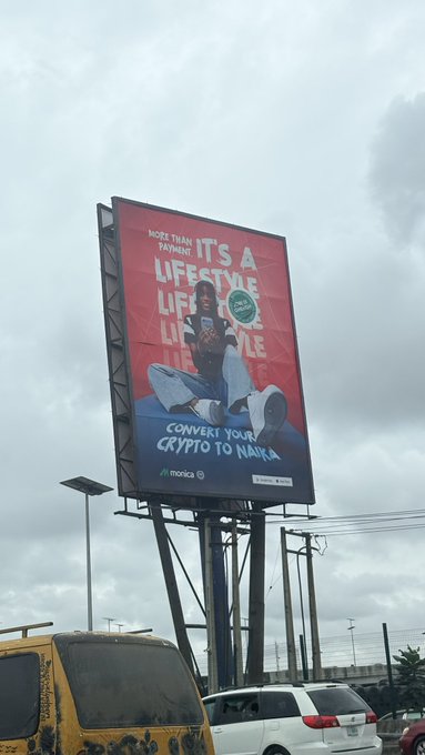 A roadside billboard advertisement featuring a woman sitting on a giant coin with text 'MORE THAN ANY PAYMENT. IT'S A LIFESTYLE' and 'CONVERT YOUR CRYPTO TO NAIRA', branded with the 'moniepoint' logo.