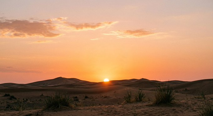 The image shows a beautiful sunset over a desert landscape, with the sun setting behind the mountains. The sky is filled with warm hues of orange and yellow as the sun sets. In the foreground, there are some bushes and sand dunes that add to the natural beauty of the scene. The post seems to be promoting an event or gathering related to prayer, work, cooking, or a similar activity.