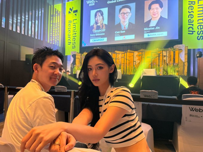 A young couple poses together at the WebX 2025 conference in Tokyo, with a "Global Leaders" panel screen behind them showing speakers Sara Shimazu (CMICROST), Can Sun, and Nicolas Jin (Gate Japan), surrounded by "Limitless Research" branding—capturing a candid moment between the post's author and Miho alongside the event's notable speakers.