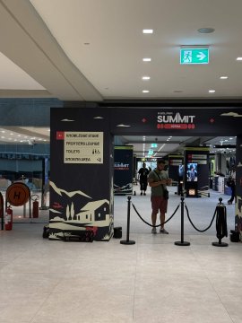 The entrance to "SUMMIT at SEA Containers" inside a modern building, with a person in red shorts walking through stanchions.