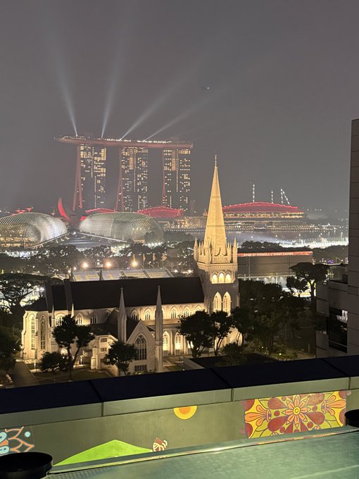 Nighttime cityscape view of Singapore, featuring the illuminated Marina Bay Sands and Esplanade Theatres, with the gothic spires of CHIJMES in the foreground.