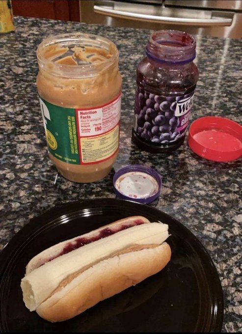 A peanut butter and jelly sandwich on a black plate sits beside an empty peanut butter jar (190 calories visible on the label) and a near-empty Welch's grape jelly jar, illustrating a "bear market" meal where someone is scraping the bottom of the barrel—literally down to the last jars of staple foods.