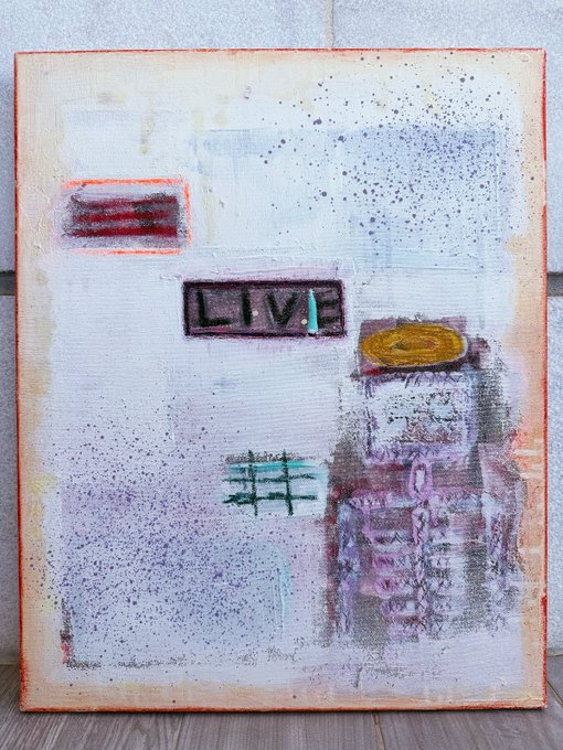 The image features a painting that says "LIVE" written in black letters, surrounded by various other colors and shapes. The artwork appears to be an abstract piece with different elements such as a yellow circle, a green square, and a red rectangle. The painting is displayed on a canvas or board, which is placed against a white wall.