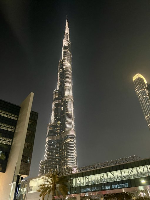 A nighttime photograph of the illuminated Burj Khalifa towering over surrounding buildings in Dubai.