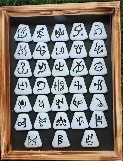 A wooden tray displaying a collection of white stones or runes, each inscribed with unique black mystical symbols and characters.