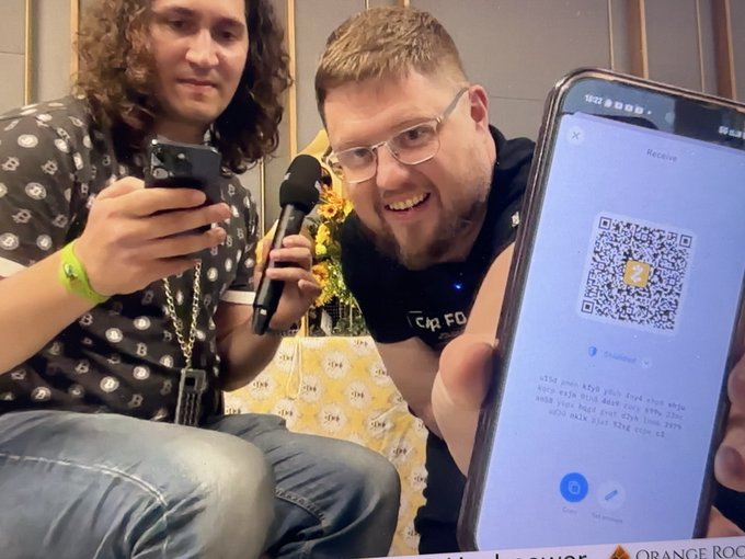 Two men are shown in a casual setting, with one holding a microphone and a phone displaying a QR code labeled "Receive" for a Zcash (Z) wallet address, while the other smiles at the camera—directly tying into the post's announcement about Peter K. Todd (known as "petertodd" in Bitcoin/crypto circles) accepting Zcash donations for his Ukraine relief efforts.