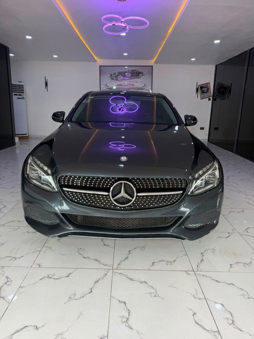 A sleek black Mercedes-Benz sedan parked in a modern showroom with white marble floors, illuminated by distinctive purple clover-shaped LED ceiling lights.