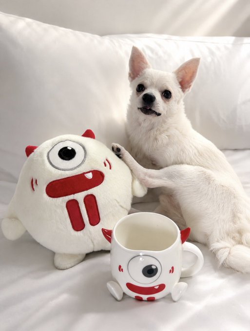 A small white dog named FerB poses with a cute white plush toy featuring a one-eyed monster design and a matching mug with the same character, all part of the TRONBull merchandise collection from TronDao_THA.