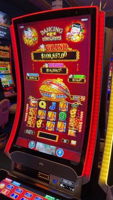 The image features a vibrant slot machine with red accents, prominently displaying an advertisement and showing the jackpot amount of $140,000. The slot machine is situated within a casino environment surrounded by various other machines. In addition, there are several chairs visible in the background around the area where people gather to play games or enjoy entertainment at the casino.