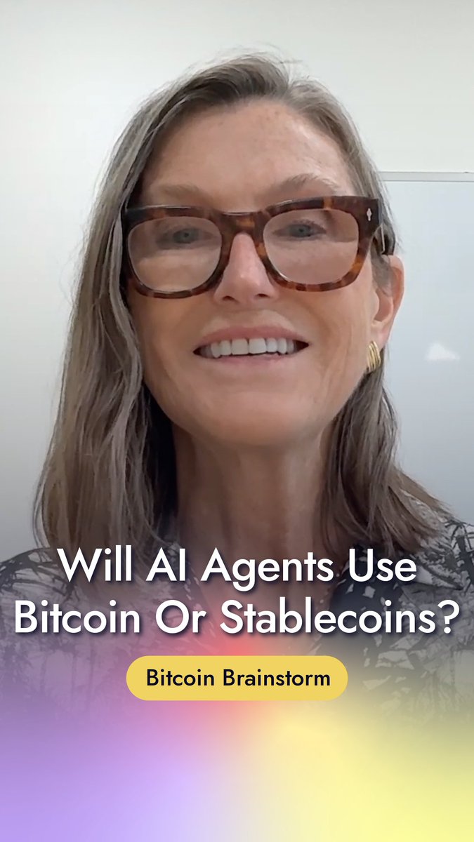 A woman wearing tortoiseshell glasses smiles at the camera, with text overlay reading "Will AI Agents Use Bitcoin Or Stablecoins?" and a yellow "Bitcoin Brainstorm" tag, visually introducing Cathie Wood's comparison of AI agent adoption of cryptocurrency to financial institutions' eventual embrace of cloud computing.