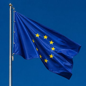 The European Union flag waves against a clear blue sky, symbolizing the regulatory authority behind the MiCA framework that is prompting Binance to suspend services for EU users. The image visually reinforces the post's theme of regulatory tension, as the EU's iconic stars-and-blue design represents the very jurisdiction enforcing the new crypto rules that Binance failed to comply with.