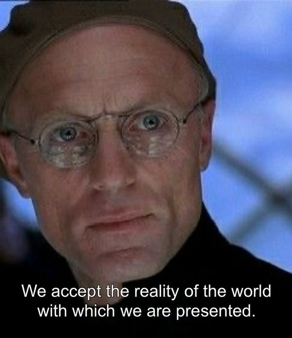 Close-up of a bespectacled older man wearing a beanie, with the subtitle "We accept the reality of the world with which we are presented."