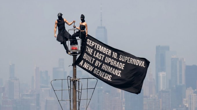 Two masked figures stand atop a pole in front of a city skyline, unfurling a banner that reads: 'SEPTEMBER 10. SUPERNOVA. THE LAST UPGRADE BUILT BY HUMANS. A NEW GENESIS.'