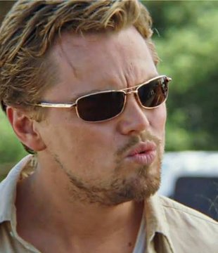 A close-up photo of a blonde man with stubble wearing aviator sunglasses and a tan shirt, appearing to be in a vehicle with greenery in the background.