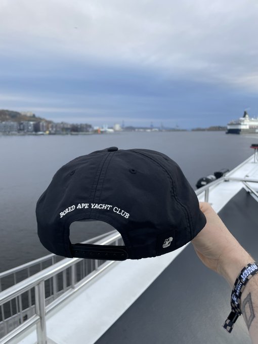The image features a person wearing a black baseball cap with white text that reads "Bored Ape Yacht Club". They are holding the hat over their head, possibly posing for a photo or showing off their new accessory. The background of the image shows a boat on the water and a pier in the distance, suggesting that this scene takes place near a body of water where boats might be docked or sailing.

The caption "GM // Bored Ape Yacht Club" is likely related to the hat's design or brand, possibly indicating that it was made by GM or produced by GM. The post seems to be promoting an interest in boat-related activities and leisurely pursuits, as suggested by the hat's design and the presence of a boat on the water.
