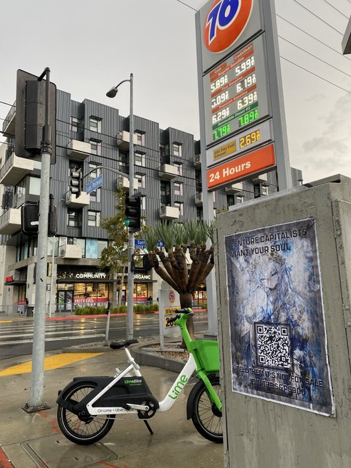 A street scene featuring a 76 gas station sign displaying fuel prices in San Francisco, with a Lime and Wheels e-bike parked next to a concrete pillar holding a poster that reads "VENTURE CAPITALISTS WANT YOUR SOUL" with a QR code.