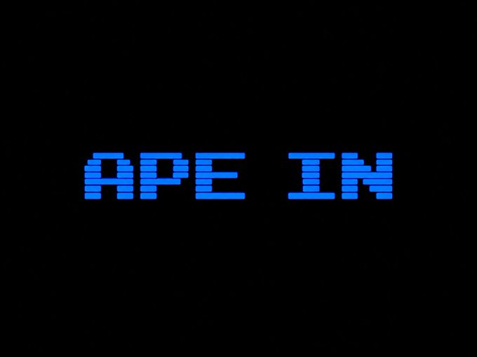A pixelated blue retro-style graphic reads 'APE IN' against a black background.
