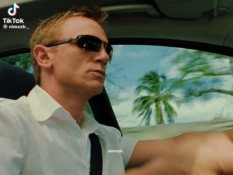 The image shows a man wearing sunglasses, sitting inside a car with his arm out the window. He appears to be driving or riding in the car while looking at something outside of the vehicle. The photo has been edited to include a caption that reads "laser focus. Let's buy neet and never work again." This suggests that there might have been some editing done on the image, possibly for promotional purposes or to convey a specific message related to the post.
