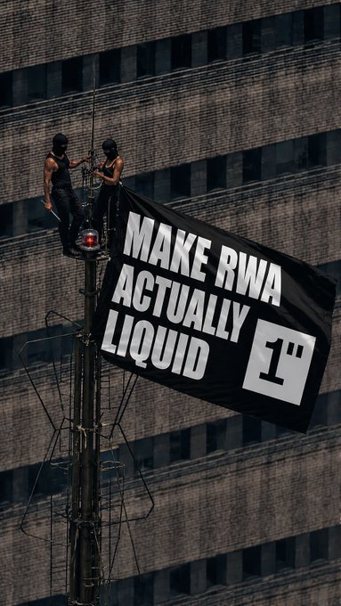Two activists scale a communications tower to unfurl a large black flag reading "MAKE RWA ACTUALLY LIQUID" alongside a logo, staging a bold protest demanding real-world asset tokenization projects achieve true market liquidity — echoing the crypto community's "GM" (good morning) greeting with a rallying cry for tangible financial progress.