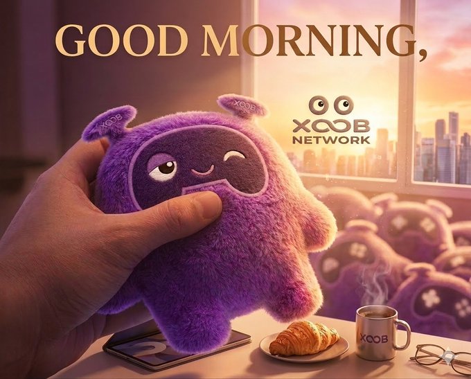 The image features a hand holding up a purple stuffed animal, which appears to be a cute monster or plush toy. The background of the image shows an urban cityscape with buildings visible through a window. There are also other objects present in the scene, such as a cup and a plate on a table near the window. The post includes text that reads "Good Morning X fam! Can i get a GM back? The web3 future is bright with @XOOBNetwork and @useTria leading the way." This suggests that the image might be related to a social media post or advertisement promoting a new product, service, or idea.