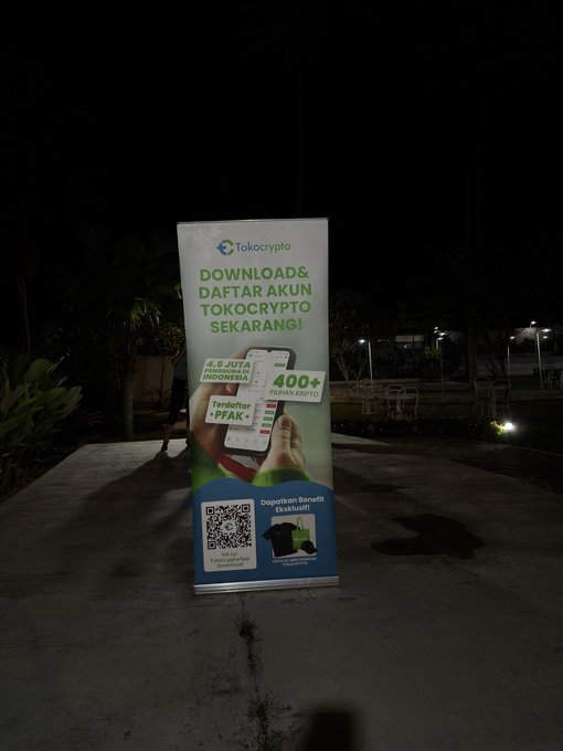 A promotional banner standee for 'Tokocrypto' displayed outdoors at night. The Indonesian text reads 'DOWNLOAD & DAFTAR AKUN TOKOCRYPTO SEKARANG!' advertising '4.5 JUTA PIALA INDONESIA' and '400+ PILIHAN KRIPTO'.