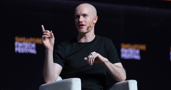A bald man wearing a black t-shirt and headset microphone speaks while gesturing, with 'SINGAPORE FINTECH FESTIVAL' visible in the background.