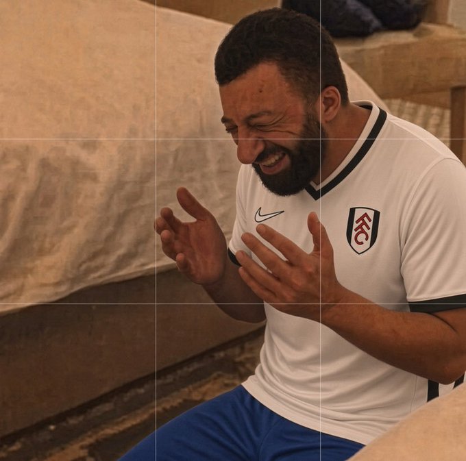 A bearded man wearing a white Fulham FC Nike soccer jersey with the FFC crest smiles broadly with his hands raised in a joyful gesture.