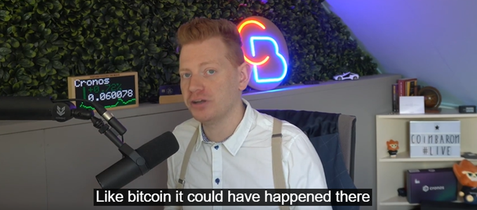 A man with reddish hair and a white shirt speaks into a microphone in a room with greenery, a Cronos ticker showing 0.068078, and a neon 'B' sign, with subtitles reading 'Like bitcoin it could have happened there'.