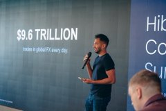 A man giving a presentation, with text on a screen behind him reading '$9.6 TRILLION trades in global FX every day.'