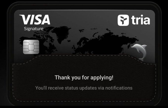 The image shows a black Visa credit card with white text that reads "Visa Signature" and "Tria", which indicates that the card belongs to Tria, an ecosystem designed for seamless access to blockchain services. The card also has a message on it encouraging users to apply for a signature, suggesting that the card is being used as a digital wallet or payment method.