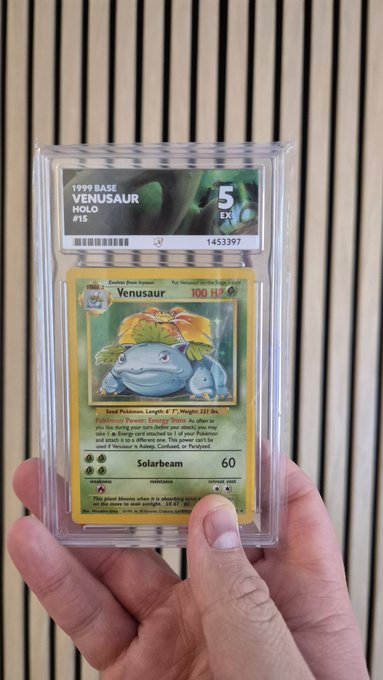 A hand holds a graded 1999 Base Set Holo Venusaur (#15) Pokémon card, which has received a PSA 5 (EX) grade with certification number 1453397.