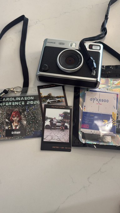 A Fujifilm Instax Mini 90 Neo camera displays a developed instant photo taken at the "CarolinaEon Conference 2020," surrounded by event swag including an "SPX6900" card and a lanyard labeled "Grillape" in a style that ties into the post's "#spx6900" reference and South Carolina gathering.