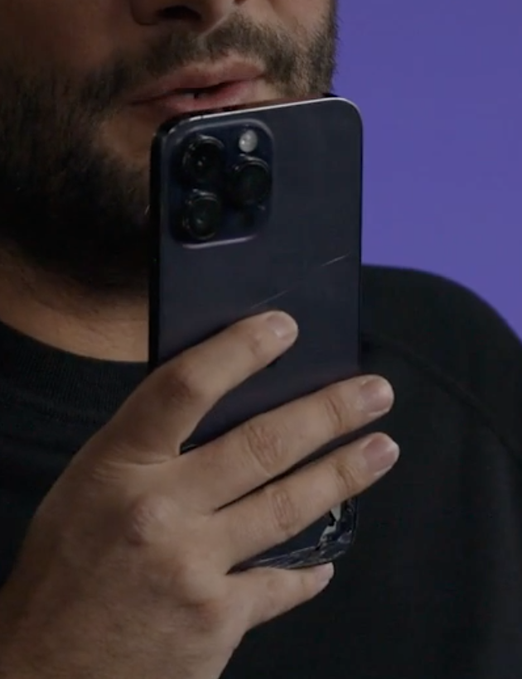 A bearded man holds a cracked purple iPhone with a triple-camera system in front of his face against a purple backdrop, visually echoing the post's theme of "broken phone" paired with a "$40m seed" announcement.