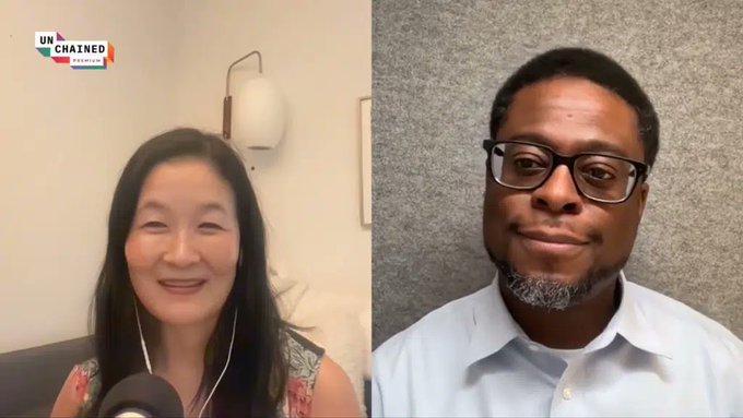 A split-screen video call from the Unchained show featuring a woman with long black hair and a man with glasses and a goatee in a light blue shirt.